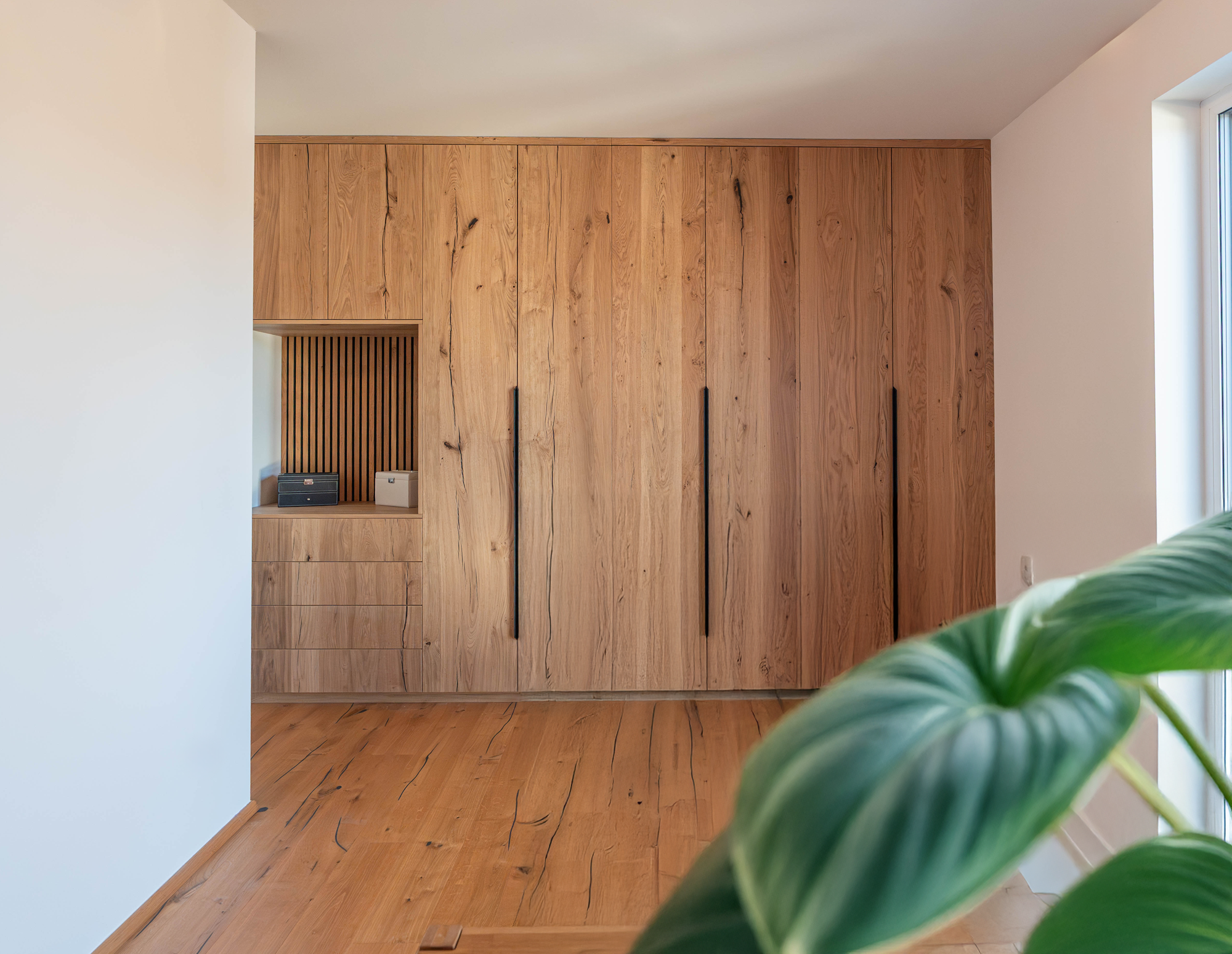 Wandfüllender maßgefertigter Einbauschrank aus rustikaler Eiche mit langen schwarzen Griffen, Schubladen und offener Nische.