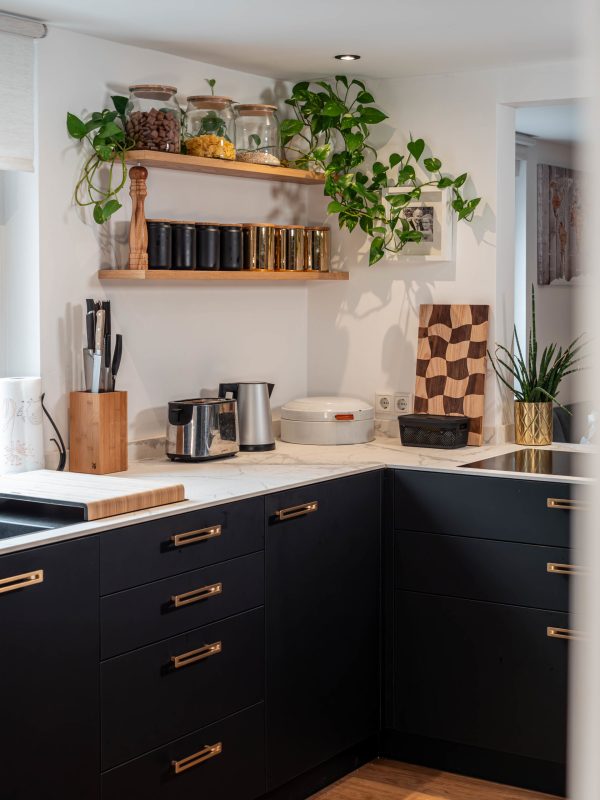 Keuken in mat zwart met gouden handgrepen en werkblad in wit graniet